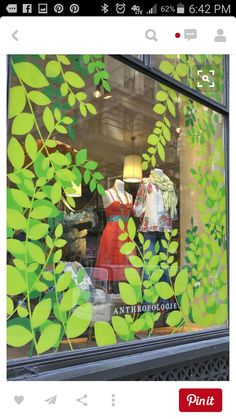 an image of a store window with green leaves on the front and side windows, showing mannequins dressed in dresses