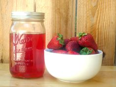 a bowl of strawberries sitting next to a jar of strawberry juice on a table