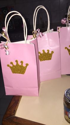 three pink bags with gold crowns on them sitting on a table next to a jar of peanut butter