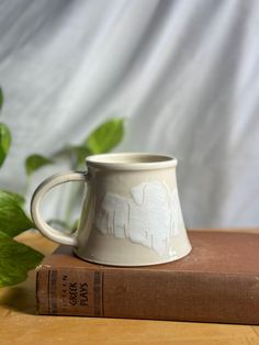 a coffee cup sitting on top of a book next to a green leafy plant