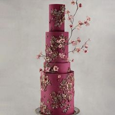 a three tiered pink wedding cake with flowers on the top and bottom, sitting on a metal stand