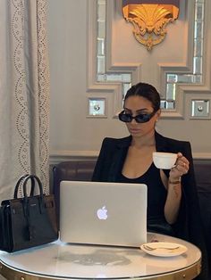 a woman sitting at a table with a laptop and coffee cup in front of her