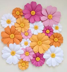 colorful paper flowers arranged on the floor for wall decoration or backdrop, including pink, orange and white daisies