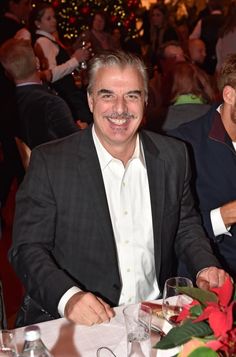 a man sitting at a table in front of a christmas tree with other people around him