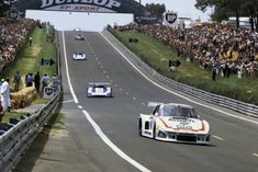 two cars driving down a race track with people watching from the sidelines behind them