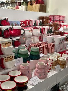 many cups and mugs are on display in a store with red ribbon around them