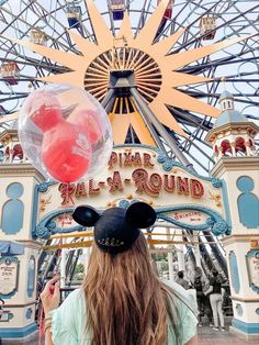 a girl with long hair wearing mickey mouse ears in front of an amusement park entrance