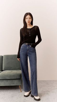 a woman standing in front of a couch wearing high waist jeans and a black shirt