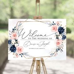 a welcome sign on an easel with flowers and greenery in the back ground