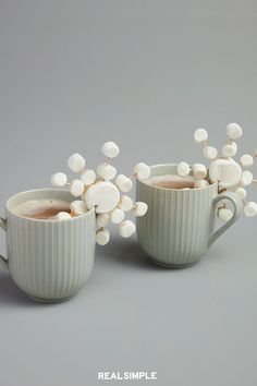 two mugs filled with hot chocolate and marshmallows on a gray background