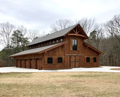 a large wooden barn sitting on top of a grass covered field in front of trees