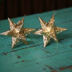 two gold star shaped ornaments sitting on top of a green wooden table next to each other