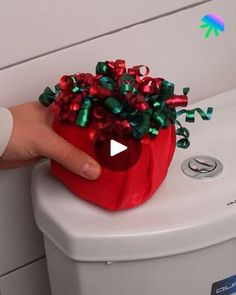 a hand is touching the top of a red box with green and red bows on it