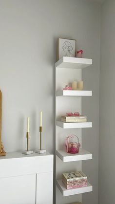 a white shelf with candles and books on it next to a dresser in a room