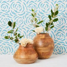 two wooden vases with white flowers and green leaves in front of a blue wall