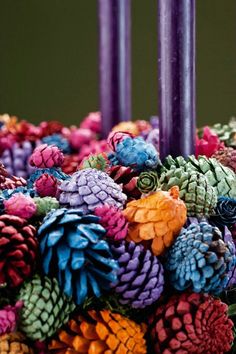 two candles are lit with pinecones and other colorful decorations in front of them