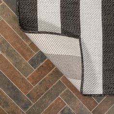 a black and white rug sitting on top of a wooden floor next to a brick wall