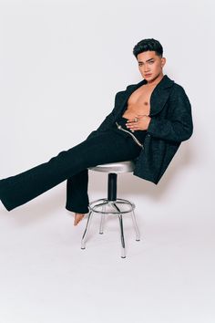 a man sitting on top of a stool with his shirt open and pants rolled up