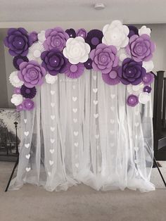 purple and white paper flowers are hanging on the wall in front of a sheer curtain