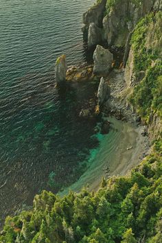 an aerial view of the ocean and rocky coastline with green trees on both sides, looking down