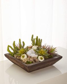 an arrangement of succulents and other plants in a wooden bowl on a table