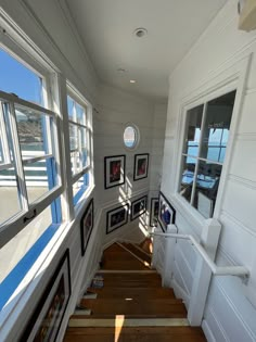 an empty hallway with framed pictures on the wall and wooden stairs leading to another room