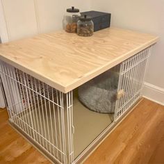 a cage with a cat in it sitting on top of a wooden table next to a door