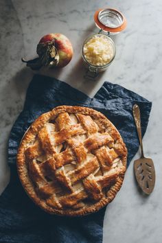 an apple pie sitting on top of a blue towel next to some apples and butter