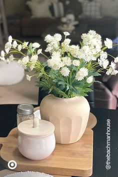 white flowers in a vase sitting on a table next to a plate and glass jar