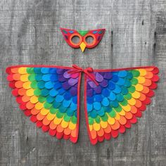 a colorful bird made out of paper on top of a wooden wall next to a pair of scissors