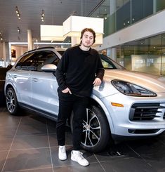 a man standing next to a silver porsche cayenne in a car showroom