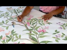 a woman is painting flowers on a white table cloth with green leaves and pink flowers