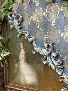 an ornate mirror with vines growing on the wall next to it and a woman's reflection in the mirror