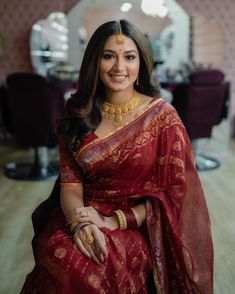 a woman in a red and gold sari sitting on a chair smiling at the camera