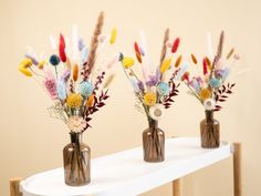 three vases filled with flowers on top of a white table next to a wall