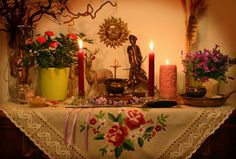 a table topped with candles and flowers on top of a tablecloth covered in lace