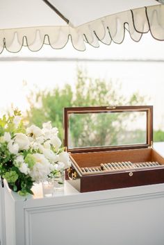 an open wooden box sitting on top of a table next to white flowers and greenery