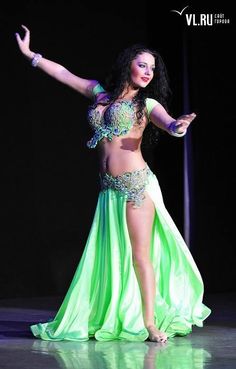 a woman in a belly dance outfit on stage with her arms out to the side