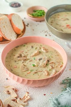 a pink bowl filled with soup next to two slices of bread on top of a table