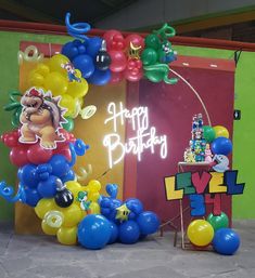 a birthday party with balloons and decorations in front of a neon sign that says happy birthday