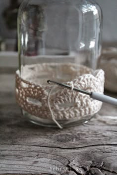 a crocheted headband sitting on top of a wooden table next to a jar