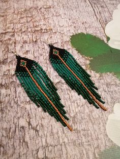 two pairs of green beaded earrings sitting on top of a wooden table next to flowers