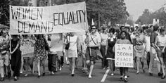 black and white photo of people marching down the street holding signs that read women, gender, equality