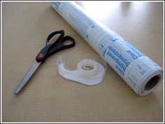 a pair of scissors and tape sitting on top of a table next to a roll of paper