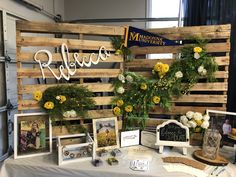 a table topped with pictures and flowers on top of a wooden pallet wall next to a sign