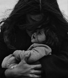 a black and white photo of a woman holding a baby in her arms with long hair