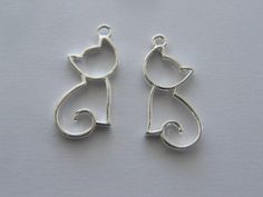 two silver cat charms sitting on top of a white surface with one facing the camera