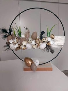 an arrangement of eggs, feathers and grass in a circular metal holder on a table