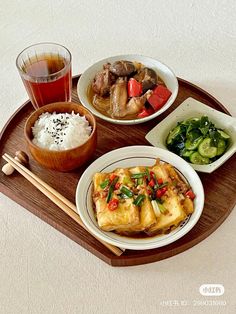 a wooden tray topped with plates and bowls filled with different types of food next to chopsticks