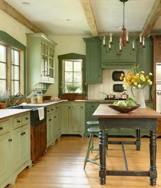 a large kitchen with green cabinets and wooden flooring, an island table surrounded by stools